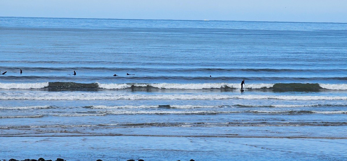 Surfer finishing a hip high wave in front of the shop as others paddle for position in the background